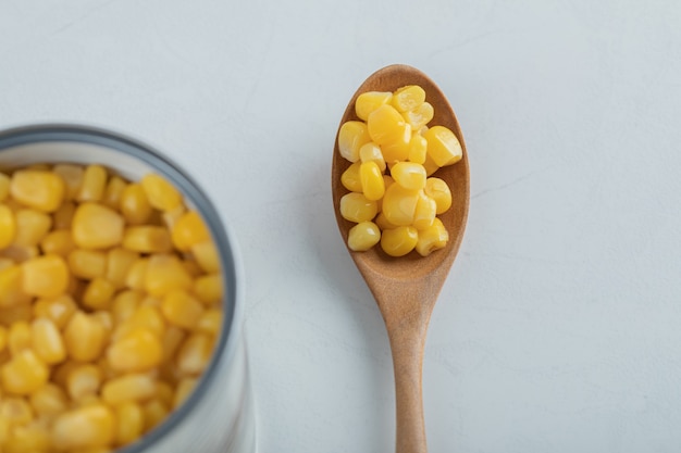 Una cuchara de madera llena de semillas de palomitas de maíz en blanco.