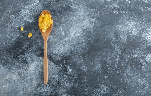 Una cuchara de madera llena de semillas de palomitas de maíz en mármol.