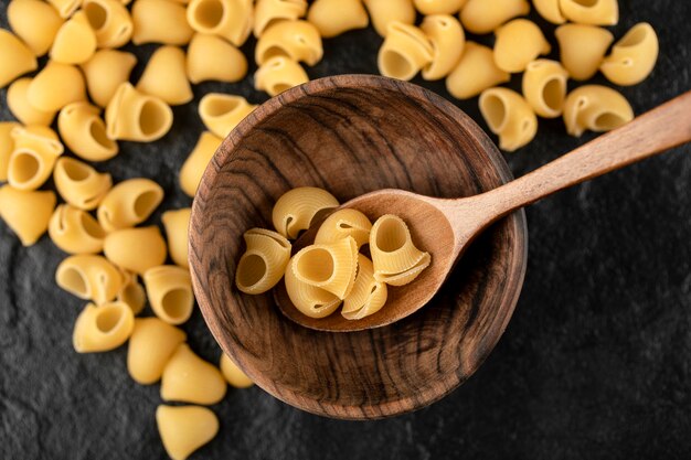 Una cuchara de madera de macarrones conchiglie crudos.