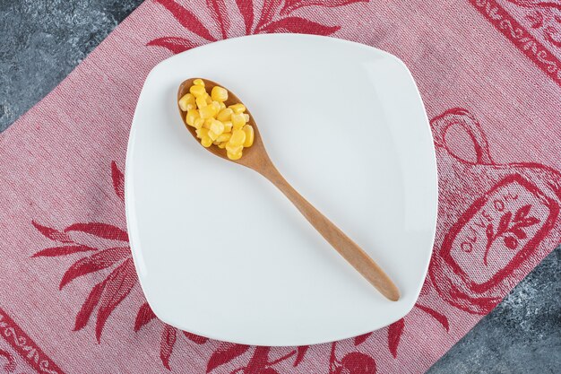 Una cuchara de madera de semillas de palomitas de maíz en un plato vacío.