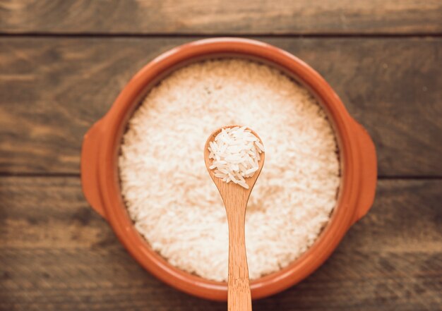 Cuchara de madera sobre el tazón de arroz crudo en la mesa de madera