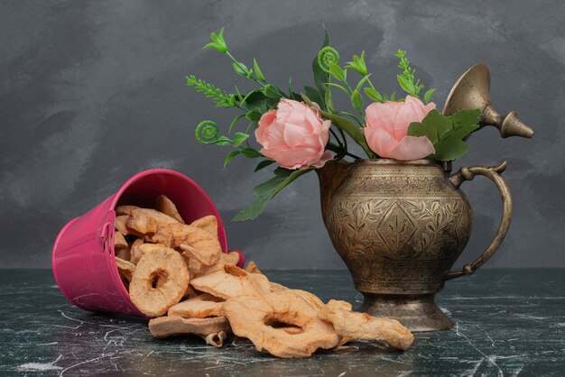 Cuchara rosa con manzana seca y jarrón de flores sobre mesa de mármol