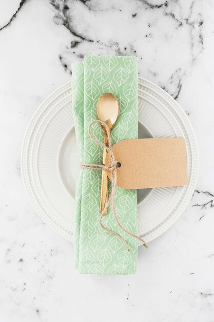 Foto gratuita cuchara y servilleta doradas atadas con una cuerda en un plato blanco sobre fondo texturizado