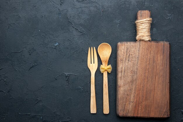 Cuchara y tenedor de madera de la tabla de servir de madera de la vista superior en el espacio de copia de la mesa oscura