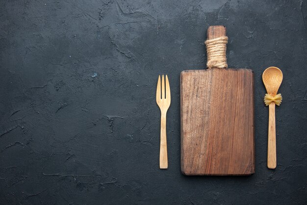 Cuchara y tenedor de madera del tablero de madera de la porción de la vista superior en lugar oscuro de la copia de la mesa