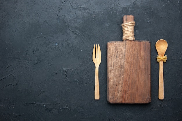 Cuchara y tenedor de madera del tablero de madera de la porción de la vista superior en lugar oscuro de la copia de la mesa