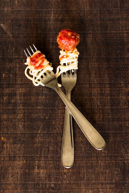 Cucharas de acero inoxidable cruzadas con albóndigas y trenette en mesa de madera