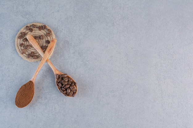 Cucharas de madera de granos de café tostados y molidos en la mesa de piedra.