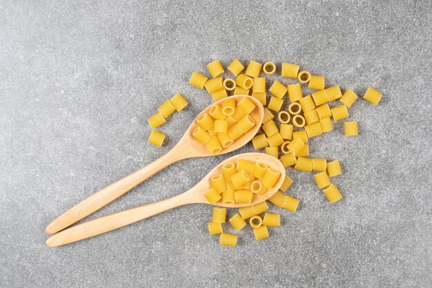 Cucharas de madera de tubo de pasta cruda sobre superficie de mármol