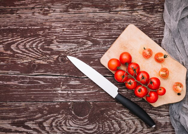 Cuchillo afilado y tomates cherry en una tabla de cortar sobre la superficie de madera