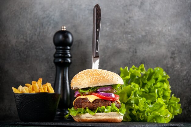 Cuchillo en delicioso sándwich de carne y papas fritas verdes en bandeja negra sobre superficie gris