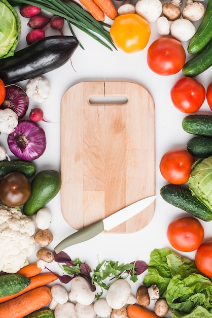 Cuchillo y tabla de cortar en medio de verduras