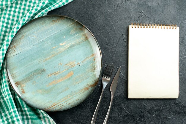 Cuchillo y tenedor de la libreta del mantel verde y blanco del plato redondo de la vista superior en el cuadro negro