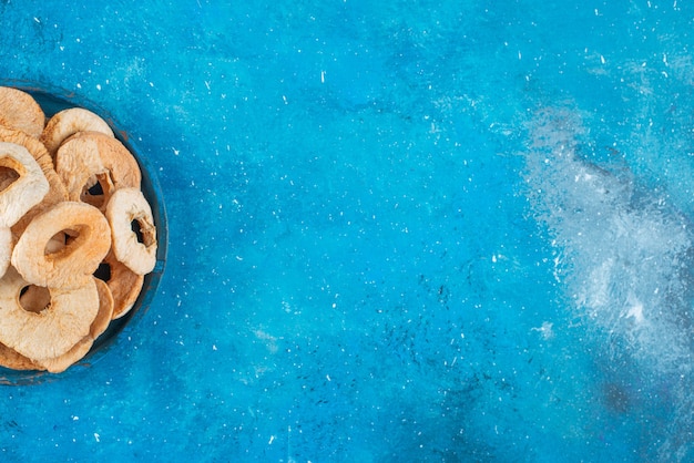 Un cuenco de anillos de manzana seca sobre la superficie azul