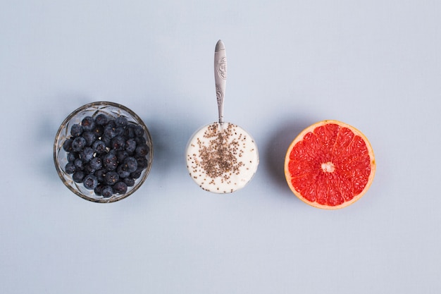 Cuenco de arándanos; pomelo rojo a la mitad y yogur con semillas de chia sobre fondo gris