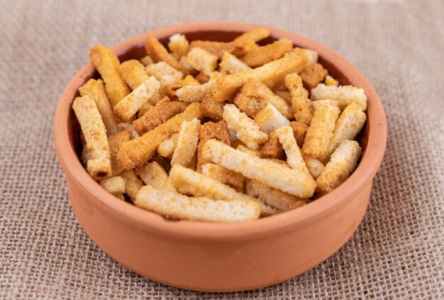 Un cuenco de arcilla con palitos de pan sobre una tela de saco