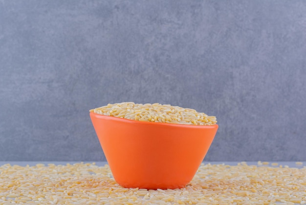 Cuenco de arroz lleno sentado sobre una masa dispersa de arroz integral sobre la superficie de mármol