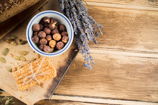 Foto gratuita cuenco de avellana; barra de lavanda y sésamo atada con una cuerda en una tabla de cortar