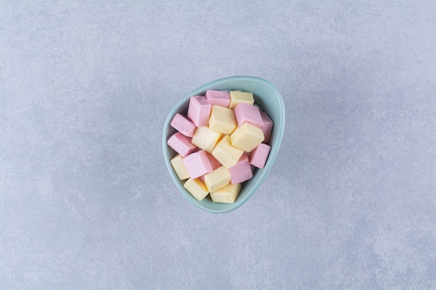Foto gratuita un cuenco azul lleno de pastelería dulce rosa y amarilla pastila