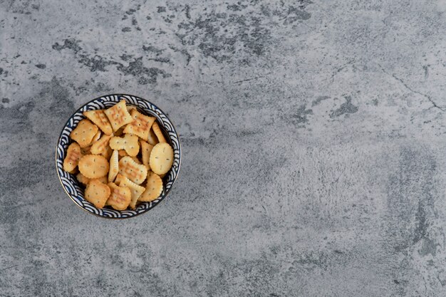 Cuenco azul lleno de varias galletas saladas sobre fondo de mármol.