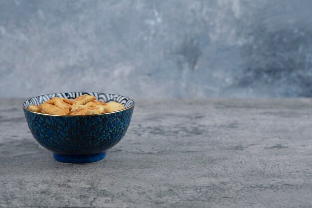 Cuenco azul lleno de varias galletas saladas sobre fondo de mármol.