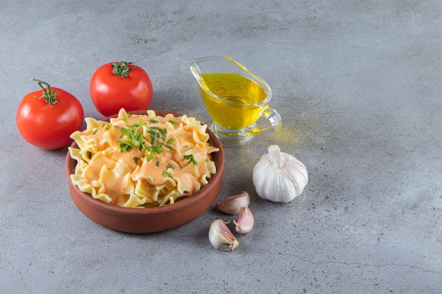 Cuenco de barro de deliciosos macarrones cremosos con aceite y verduras sobre fondo de piedra.