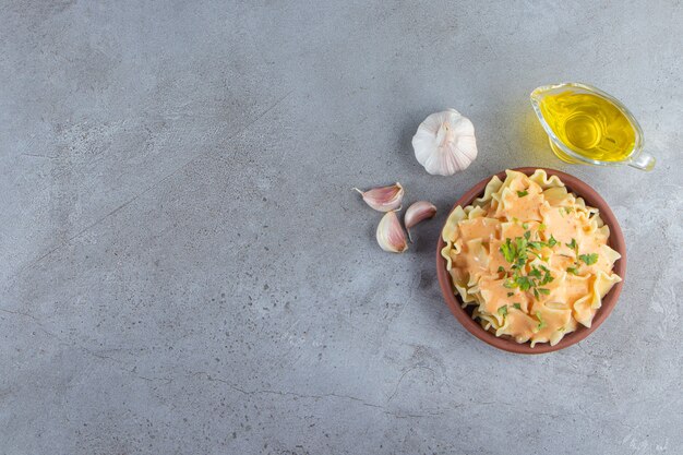 Cuenco de barro de deliciosos macarrones cremosos con aceite y verduras sobre fondo de piedra.