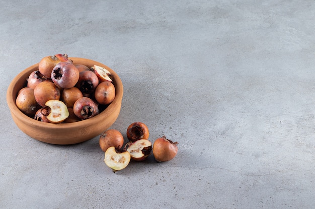 Foto gratuita cuenco de barro lleno de frutos de níspero maduros sobre fondo de piedra.