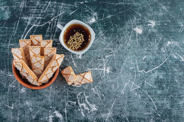 Un cuenco de barro lleno de gofres dulces se pega con una taza de té negro.