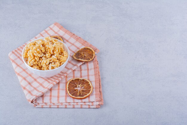 Cuenco blanco de caramelos duros con nueces y rodajas de limón sobre piedra.