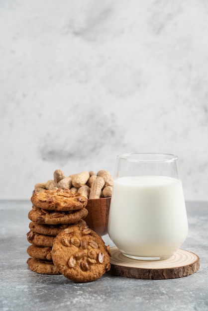 Cuenco de cacahuetes, vaso de leche y galletas con cacahuetes orgánicos sobre mesa de mármol.