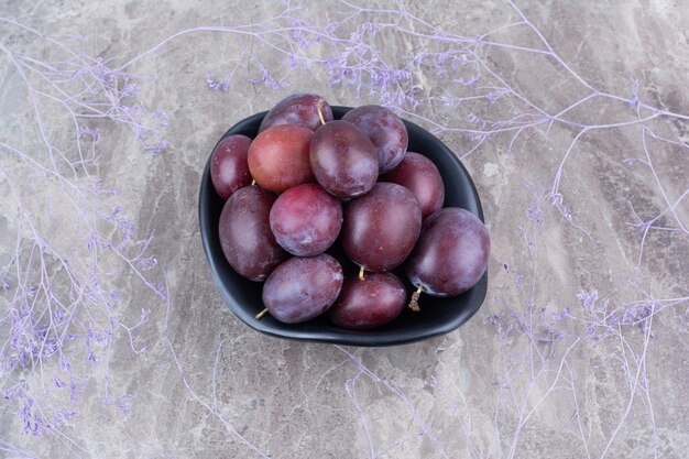 Cuenco de ciruelas maduras sobre fondo de piedra.