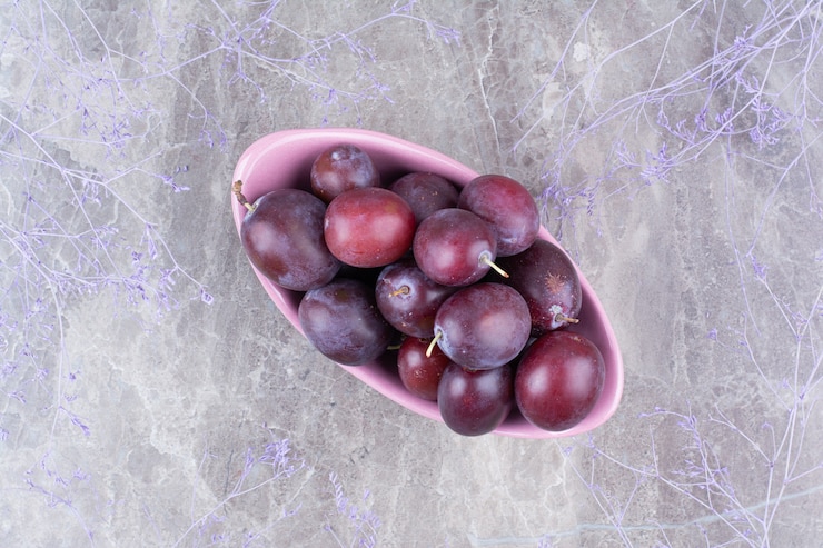 Foto gratuito cuenco de ciruelas maduras sobre fondo de piedra.