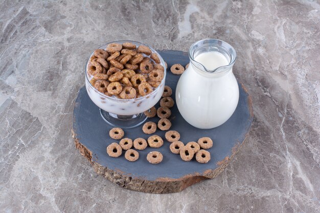 Un cuenco de cristal de yogur saludable con cereales crujientes y una jarra de cristal de leche.