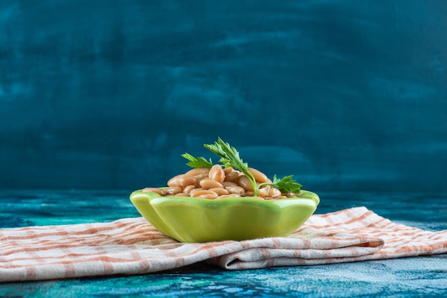 Un cuenco de deliciosos frijoles horneados sobre un paño de cocina, sobre la mesa azul.