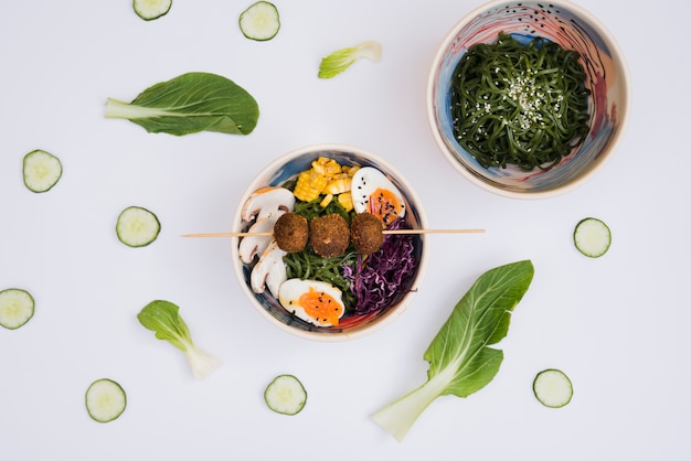 Cuenco de ensalada de algas con ramen comida asiática tradicional decorada con rodajas de pepino y hojas sobre fondo blanco