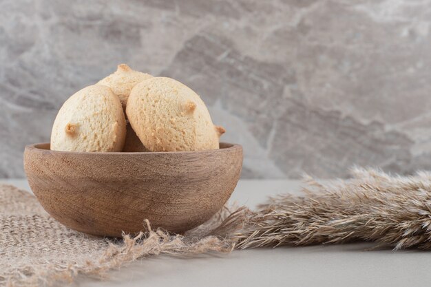 Cuenco de galletas junto a tallos de pasto sobre fondo de mármol.