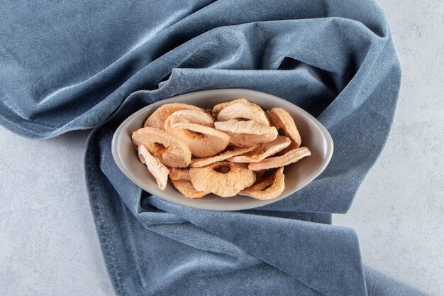 Cuenco gris de anillos de manzana secos saludables en piedra.