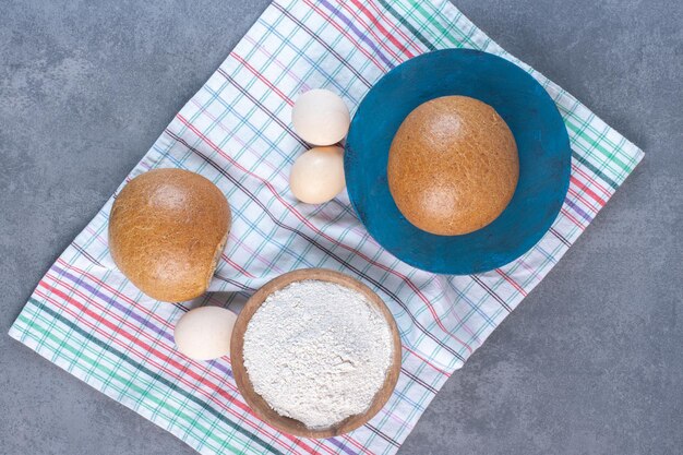 Cuenco de harina, huevos y bollos sobre una toalla sobre fondo de mármol. Foto de alta calidad