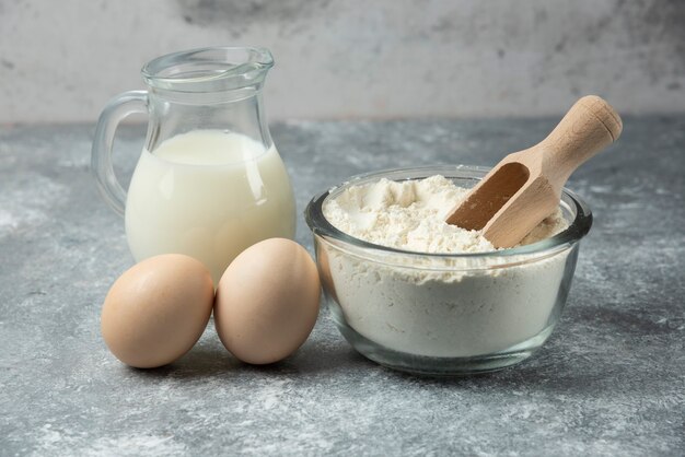 Cuenco de harina, huevos crudos y leche en la mesa de mármol.