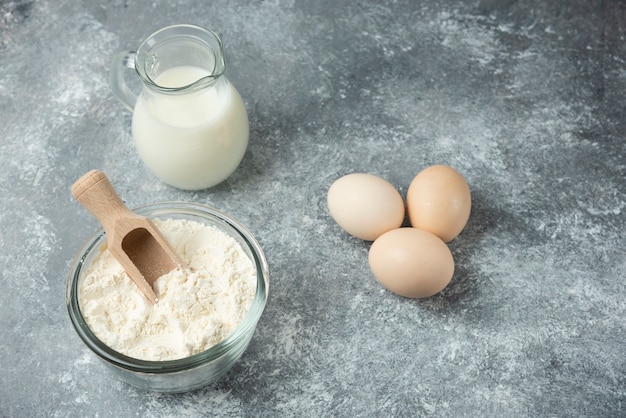 Cuenco de harina, huevos crudos y leche sobre mármol.