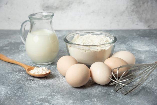 Cuenco de harina, huevos y leche sobre mármol.