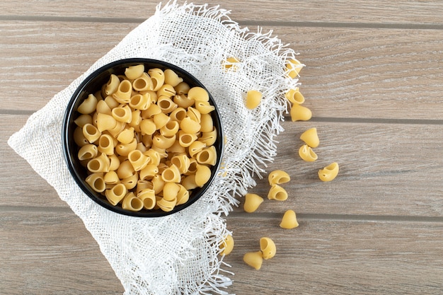 Cuenco lleno de pasta seca en mesa de madera. Foto de alta calidad