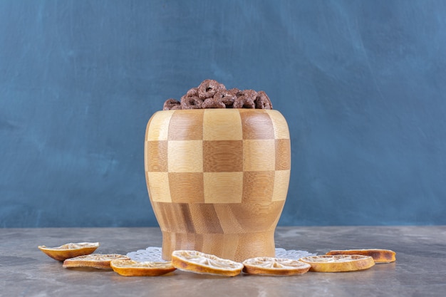 Un cuenco de madera de anillos de cereal de chocolate con rodajas de naranja seca.