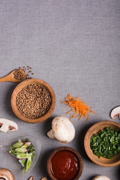 Cuenco de madera de cebolleta; semillas de cilantro; salsa; Seta y zanahoria rallada sobre mantel de lino gris