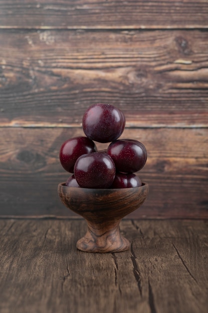 Foto gratuita un cuenco de madera con ciruelas púrpuras frescas y saludables en la mesa de madera.