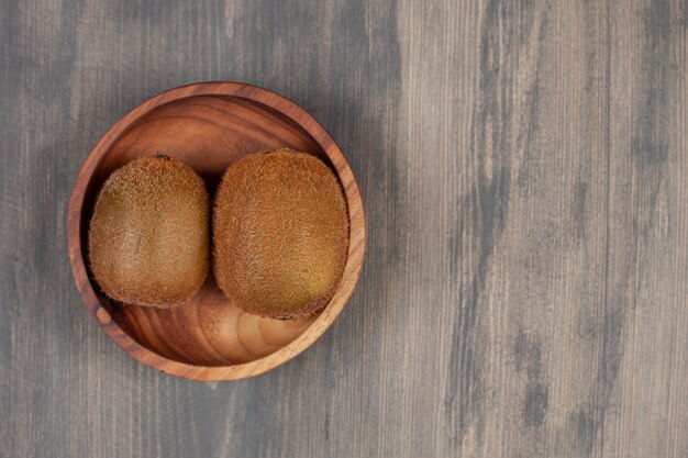 Un cuenco de madera con dos kiwis frescos sobre una mesa de madera. Foto de alta calidad