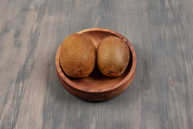 Un cuenco de madera con dos kiwis frescos sobre una mesa de madera. Foto de alta calidad