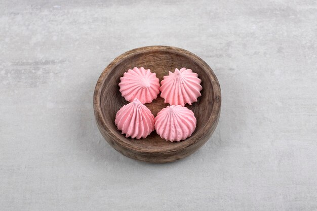 Cuenco de madera de dulces de merengue rosa sobre mesa de piedra.