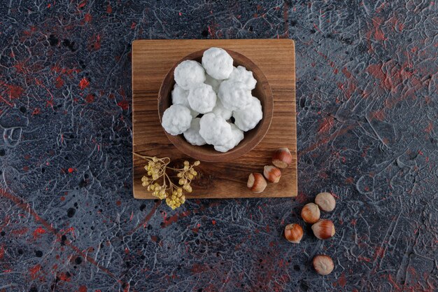 Un cuenco de madera lleno de dulces caramelos blancos con frutos secos saludables sobre una mesa oscura.